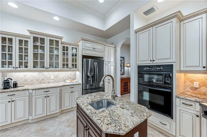 Kitchen with stainless steel fridge with ice dispenser, arched walkways, decorative backsplash, crown molding, and light stone countertops