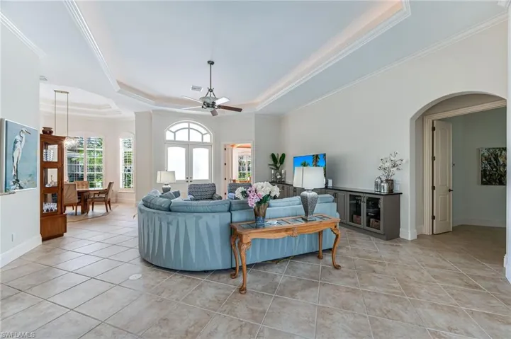 Living room featuring a raised ceiling, light tile patterned flooring, ornamental molding, a ceiling fan, and arched walkways
