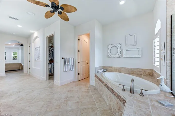 Ensuite bathroom with ceiling fan, a bath, recessed lighting, a walk in closet, and tile patterned flooring