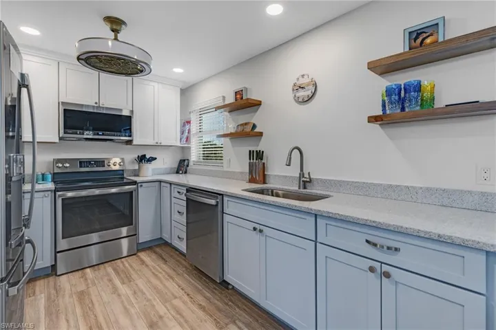 Kitchen with sink, light hardwood / wood-style flooring, appliances with stainless steel finishes, light stone counters, and white cabinetry