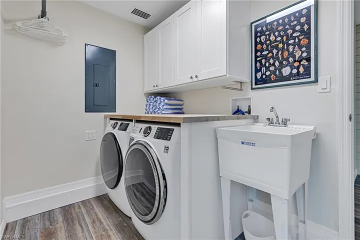 Washroom featuring electric panel, cabinets, wood-type flooring, and washing machine and dryer