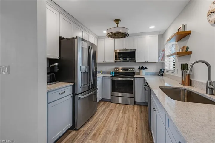 Kitchen with light stone countertops, sink, appliances with stainless steel finishes, white cabinets, and light wood-type flooring