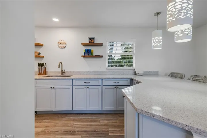 Kitchen with sink, hardwood / wood-style flooring, decorative light fixtures, light stone counters, and kitchen peninsula