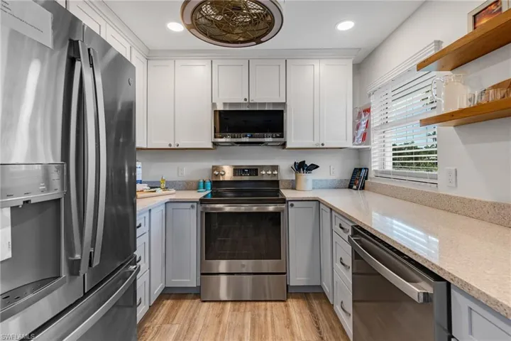 Kitchen featuring white cabinets, light hardwood / wood-style floors, light stone countertops, and appliances with stainless steel finishes