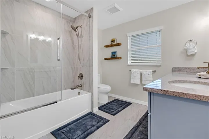 Full bathroom featuring combined bath / shower with glass door, vanity, toilet, and tile patterned flooring