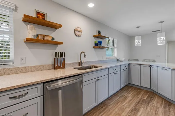 Kitchen with pendant lighting, gray cabinetry, sink, stainless steel dishwasher, and hardwood / wood-style flooring
