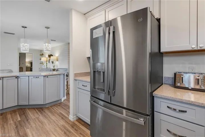 Kitchen featuring light stone countertops, stainless steel fridge, light wood-type flooring, gray cabinets, and hanging light fixtures