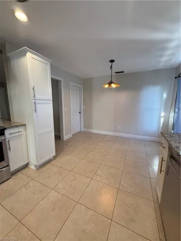 Kitchen featuring white cabinetry, light stone counters, range, dishwashing machine, and hanging light fixtures