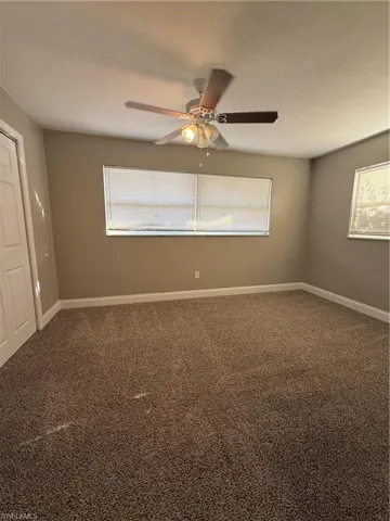 Carpeted empty room featuring baseboards and a ceiling fan