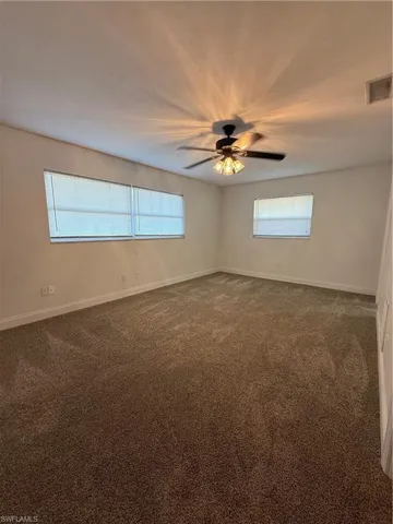 Unfurnished room featuring dark colored carpet and a ceiling fan