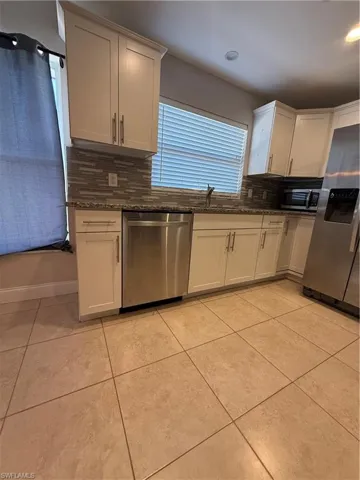 Kitchen with fridge, stainless steel dishwasher, white cabinets, dark stone counters, and recessed lighting