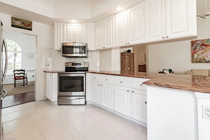Kitchen with appliances with stainless steel finishes, white cabinetry, backsplash, light tile patterned flooring, and light stone counters