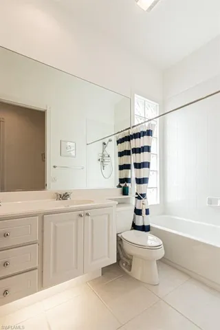 Bathroom with tile patterned flooring, shower / bathtub combination with curtain, vanity, and toilet