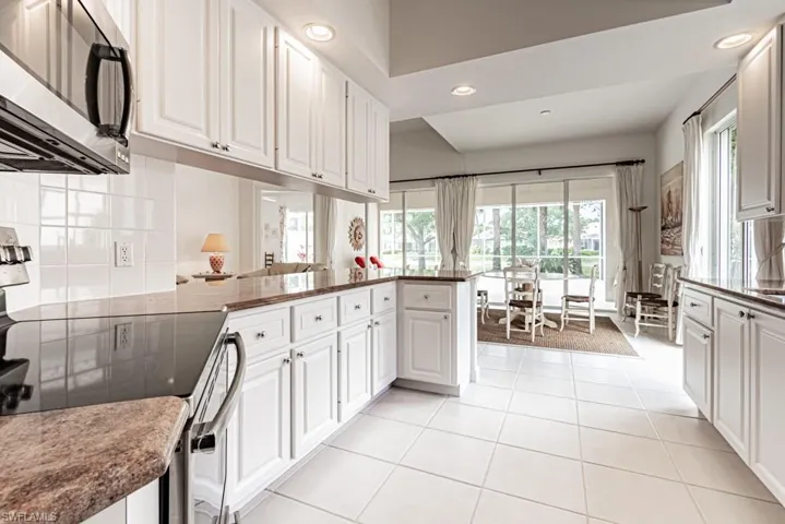 Kitchen with tasteful backsplash, light tile patterned floors, white cabinets, stainless steel microwave, and electric range
