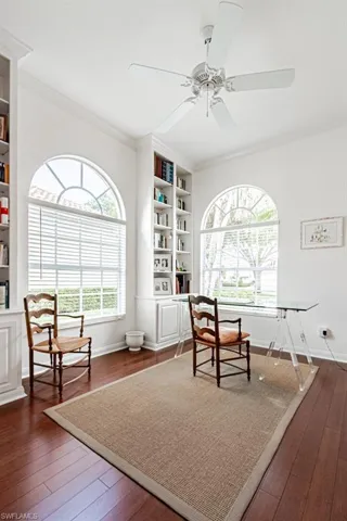 Living area with crown molding, ceiling fan, dark wood-style flooring, baseboards, and built in shelves