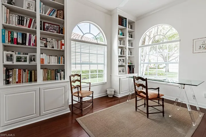 Office area with dark wood-type flooring, ornamental molding, baseboards, and built in shelves