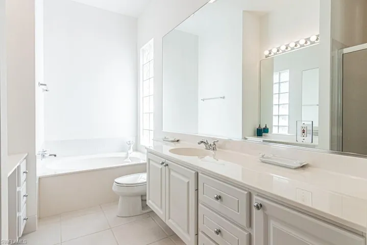 Bathroom with a bath, a shower with shower door, vanity, tile patterned flooring, and toilet