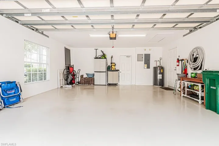 Garage with electric water heater, electric panel, freestanding refrigerator, and a garage door opener