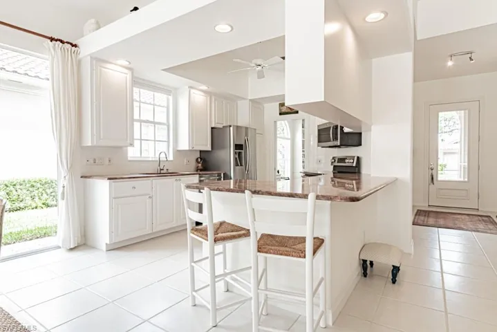 Kitchen featuring light tile patterned floors, a peninsula, a ceiling fan, appliances with stainless steel finishes, and a sink