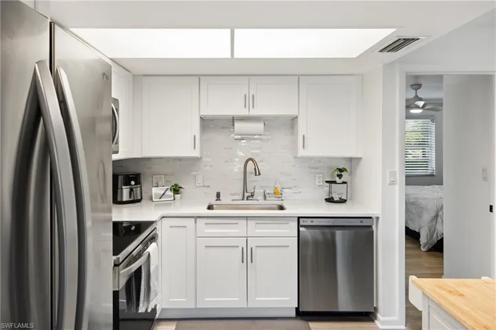 Kitchen featuring appliances with stainless steel finishes, white cabinets, decorative backsplash, light wood-style floors, and a ceiling fan