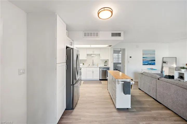 Kitchen featuring light wood-type flooring, open floor plan, appliances with stainless steel finishes, decorative backsplash, and white cabinets