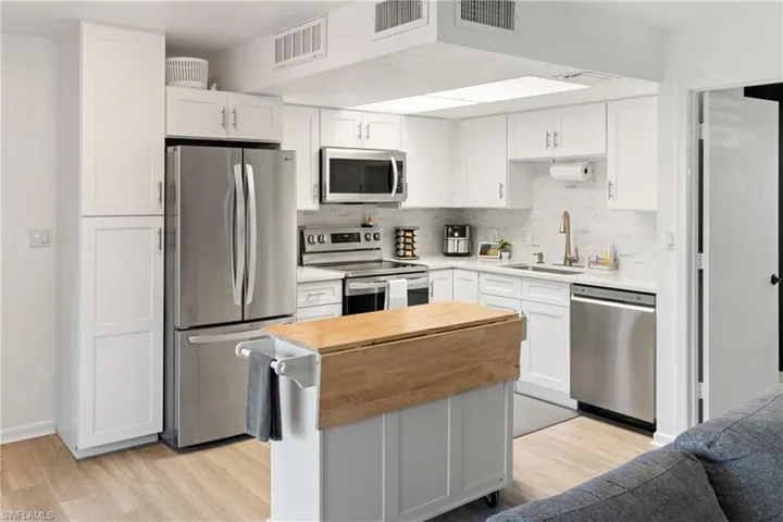 Kitchen with appliances with stainless steel finishes, white cabinets, backsplash, and a kitchen island