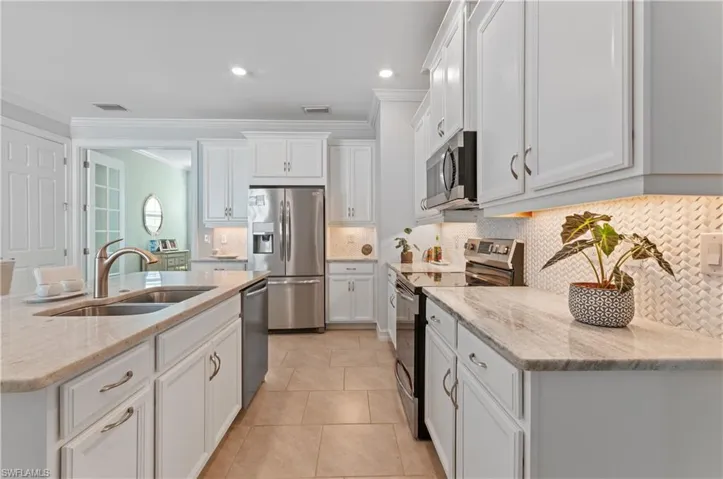 Kitchen with stainless steel appliances, sink, light tile patterned floors, decorative backsplash, and white cabinetry