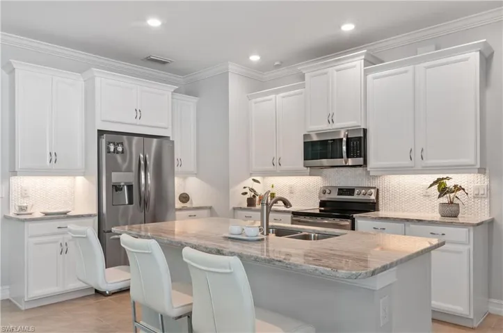 Kitchen with decorative backsplash, stainless steel appliances, light tile patterned floors, and an island with sink
