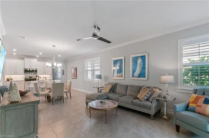 Tiled living room with crown molding and ceiling fan with notable chandelier