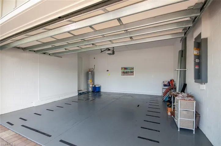 Garage featuring electric panel, a garage door opener, and water heater