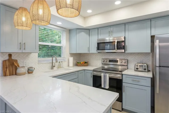Kitchen with appliances with stainless steel finishes, light stone countertops, gray cabinets, tasteful backsplash, and recessed lighting