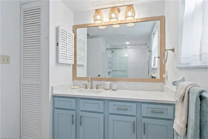 Bathroom featuring tasteful backsplash, a closet, vanity, and a shower stall