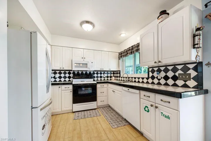 Kitchen with dark countertops, white appliances, white cabinets, and backsplash