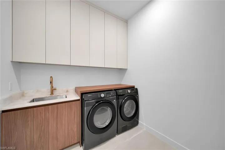 Laundry area featuring an undermount sink with a bronze-finish faucet, stone countertop, wood-finish lower cabinetry, and light-toned upper cabinetry