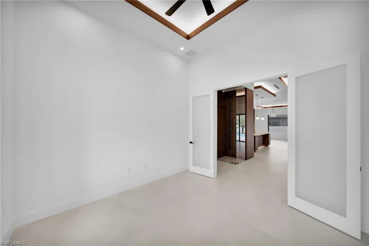 Spacious room featuring light-toned flooring, white walls, and a high ceiling with a wood-beamed detail and ceiling fan