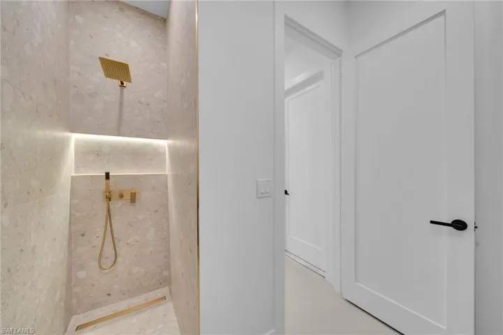 Walk-in shower featuring light-toned tile walls, a gold-finish rainfall showerhead, a handheld shower fixture, and accent lighting