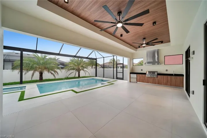 Expansive covered patio featuring a wood-finish ceiling, dual ceiling fans, and an outdoor kitchen with built-in grill and beverage refrigerator