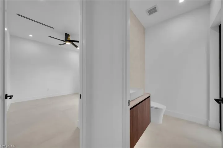 Modern powder room featuring a floating wood-finish vanity with an integrated basin, a contemporary toilet, and light-toned flooring