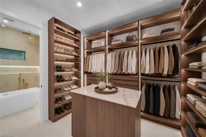 Custom closet system featuring wood-finish cabinetry, integrated lighting, and a central island with a stone countertop