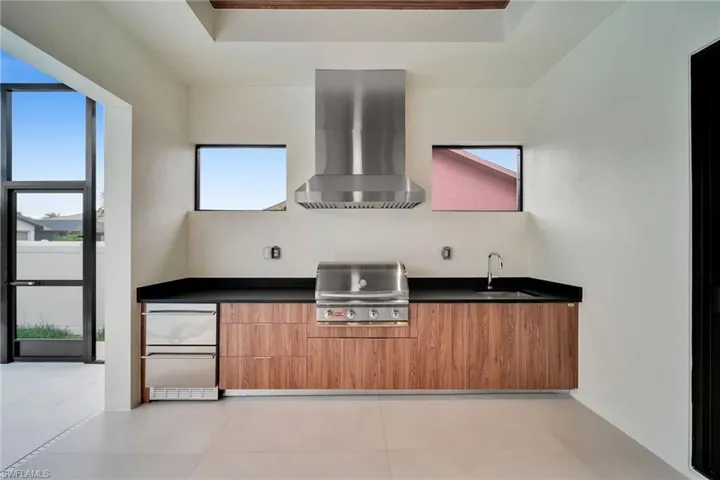 Outdoor kitchen featuring a stainless steel range hood, built-in grill, black countertop, and wood-finish cabinetry
