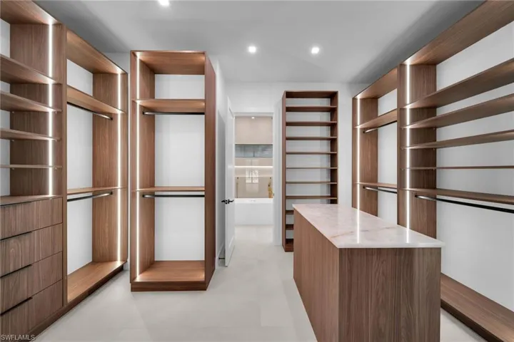 Custom closet system featuring wood-finish cabinetry, integrated LED lighting, multiple hanging rods, built-in drawer storage, and a central island with a stone countertop