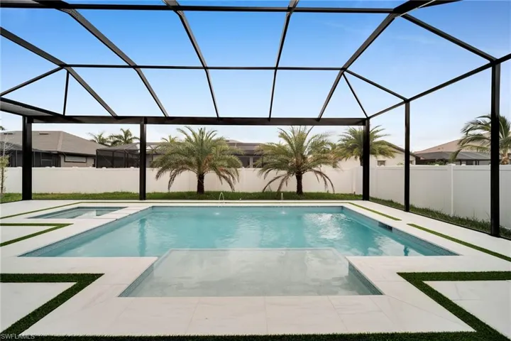 Screened outdoor living area featuring a rectangular pool with an integrated spa, expansive white tile decking, and decorative artificial turf accents