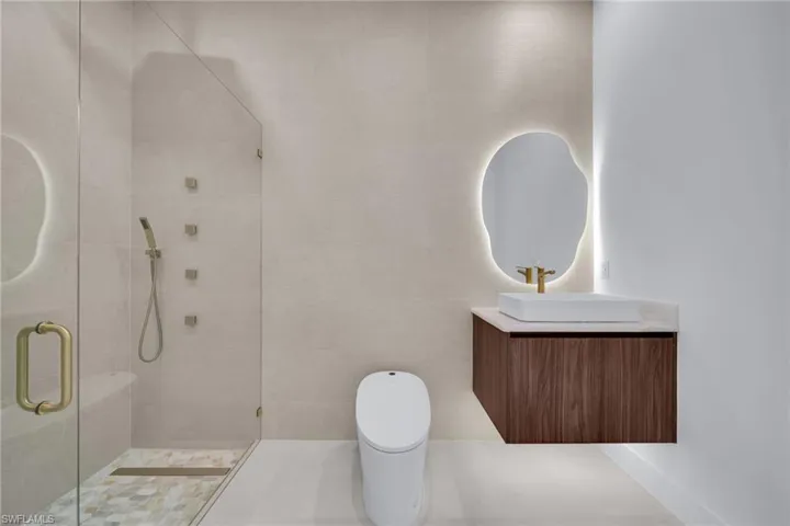Modern bathroom featuring a floating wood-finish vanity with a vessel sink, an illuminated organic-shaped mirror, and a frameless glass shower enclosure