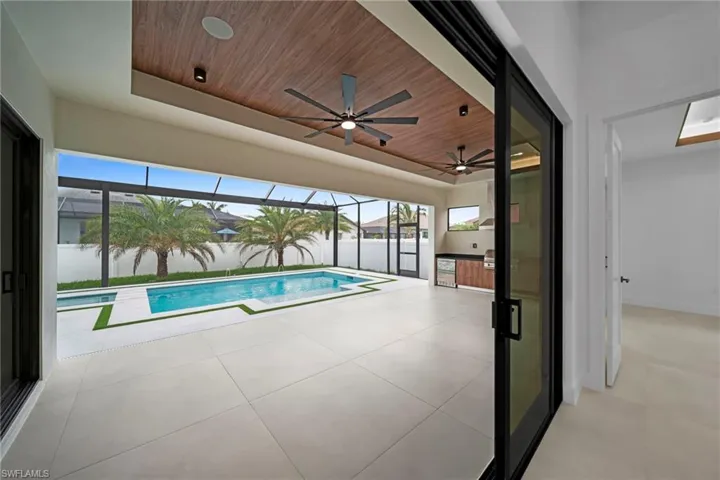 Expansive screened lanai featuring a rectangular swimming pool with integrated spa, a built-in outdoor kitchen with grill, wood-finish ceiling with integrated fans, and large format tile flooring
