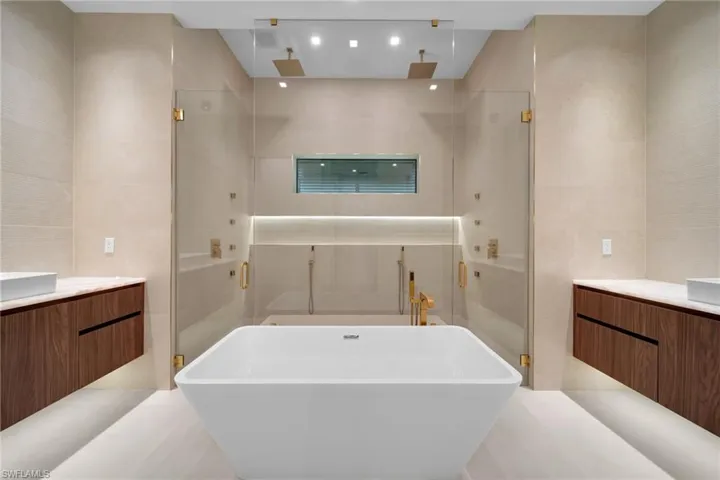 Freestanding soaking tub with a dual shower system featuring gold-tone fixtures and rain shower heads