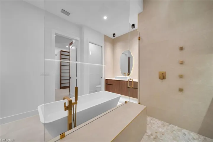 Freestanding soaking tub with gold-tone fixtures, complemented by a walk-in shower featuring a built-in bench, pebble-tile flooring, and gold-tone shower controls