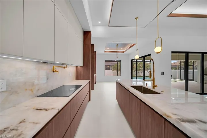 Modern kitchen featuring warm wood-finish lower cabinetry, light-toned upper cabinetry, and a full-height stone slab backsplash