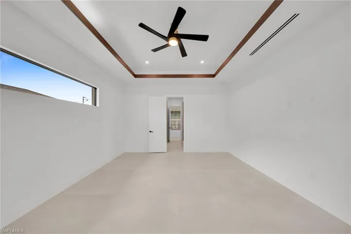 Spacious room featuring a tray ceiling with wood-finish accents, a modern ceiling fan, recessed lighting, and a high horizontal window