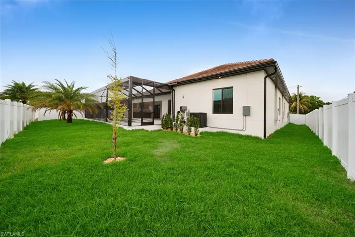 Expansive rear yard featuring a large screened patio enclosure, lush green lawn, privacy fencing, mature palm trees, and a low-profile white stucco exterior