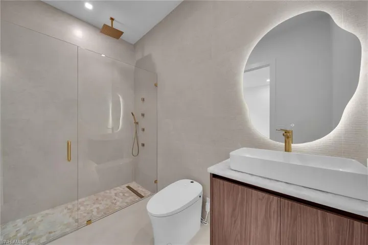 Modern bathroom featuring a frameless glass shower enclosure with a rain showerhead and multiple body jets